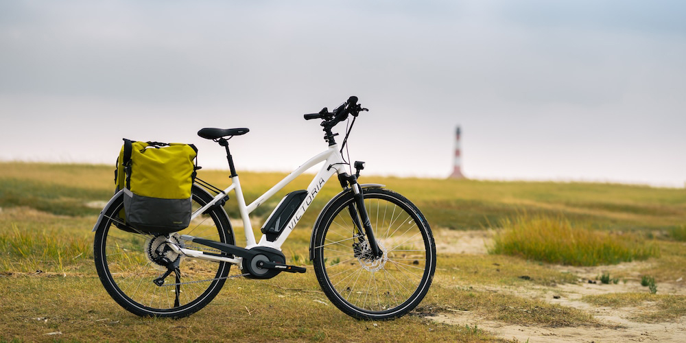 een victoria elektrische fiets staat geparkeerd in de duinen met op de achtergrond een vuurtoren